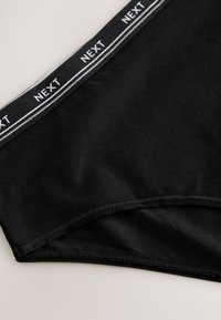 Braga negra de algodón con una suave cinturilla que lleva la marca "NEXT" y franjas blancas de acento, terminada con costuras limpias a lo largo de los bordes.