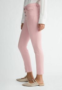 Ružové skinny džínsy s vysokým pásom, ktoré majú tri gombíky na zapínanie, bočné vrecká a hladkú, elastickú textúru látky.