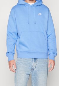 Ljusblå huva sweatshirt i mjukt tyg, med en framfickla och vit Nike-logotyp på vänster bröst.