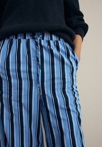 Lichtblauwe en marineblauwe gestreepte broek met een trekkoord in de taille, voorzien van zijzakken en verticale patronen op een gladde stof.
