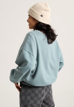 Light blue oversized sweatshirt with dropped shoulders paired with checkered gray pants; person wearing a cream ribbed beanie.