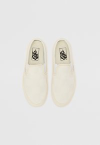 Tenisi slip-on bej cu un model în carouri. Realizați din pânză, având o parte elastică albă și o talpă din cauciuc texturat.