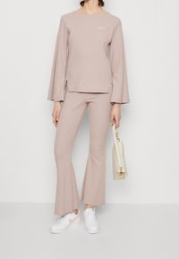 Růžový žebrovaný top s dlouhým rukávem a bočními rozparky, spárovaný s odpovídajícími žebrovanými kalhotami s širokými nohavicemi. Oblečeno s bílými teniskami a béžovou kabelkou.