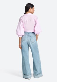 Maglietta corta rosa chiaro con maniche a palloncino e dettagli con bottoni sul retro. Indossata con jeans a gamba larga blu chiaro con risvolti.