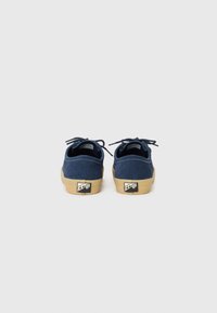 Blue suede shoes with lace closures, featuring a tan rubber sole and a logo accent on the heel. Smooth texture and classic design.
