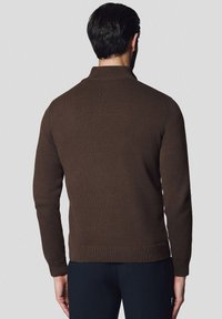 Brązowy sweter z dzianiny, z wysokim kołnierzem, prążkowanym dołem i mankietami. Tył ma dopasowany krój i teksturowany materiał zapewniający ciepło.