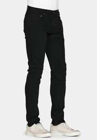 Jeans in denim nero con una vestibilità slim, dotati di chiusura a zip, cinque tasche e cuciture a contrasto, abbinati a sneakers chiare.