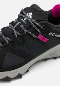 Chaussure de randonnée noire avec un dessus texturé, des lacets gris, des accents roses et une semelle extérieure en caoutchouc durable avec des grips de traction.