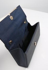 Sac en cuir bleu marine avec un extérieur texturé. Intérieur doublé d'un tissu lisse, doté d'une fermeture magnétique et de quincaillerie dorée.