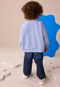 Hellblaues, übergroßes Sweatshirt mit gerippten Bündchen, kombiniert mit dunklen Denim-Jeans im Weitbein-Schnitt und cremefarbenen Sneakers mit pastellfarbenen Akzenten.