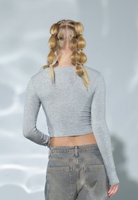 Gray long-sleeve cropped top made of soft jersey fabric, paired with high-waisted distressed blue jeans. Hair styled in multiple braids.