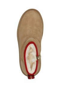 Kahva suede slipper, jossa on valkoinen karvavuori, punainen reunus avauksessa ja sivuvetoketjuyksityiskohta.