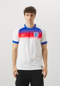 Maglia da calcio bianca a maniche corte con sfumatura rossa e blu sulla parte superiore, dotata di un colletto blu e dello stemma dell'Inghilterra sul lato sinistro del petto.