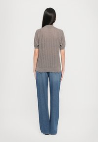 Hnedý rebrovaný pletený top s krátkymi puff rukávmi, kombinovaný s vysokými, voľnými modrými džínsami, zobrazený zozadu.