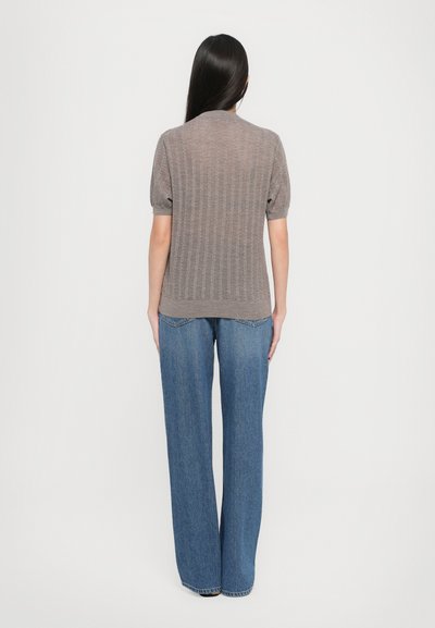 Top a righe marrone a maglia con maniche corte a sbuffo, abbinato a jeans in denim blu a vita alta e larghi, visto da dietro.