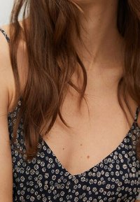 Abito blu scuro con scollatura a V, caratterizzato da piccoli motivi floreali bianchi, spalline sottili e una texture morbida.