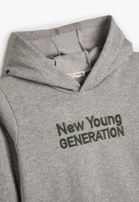 Sudadera gris con bolsillo frontal, texto bordado "Nueva JOVEN GENERACIÓN" en verde oscuro. Tejido suave con un corte relajado.