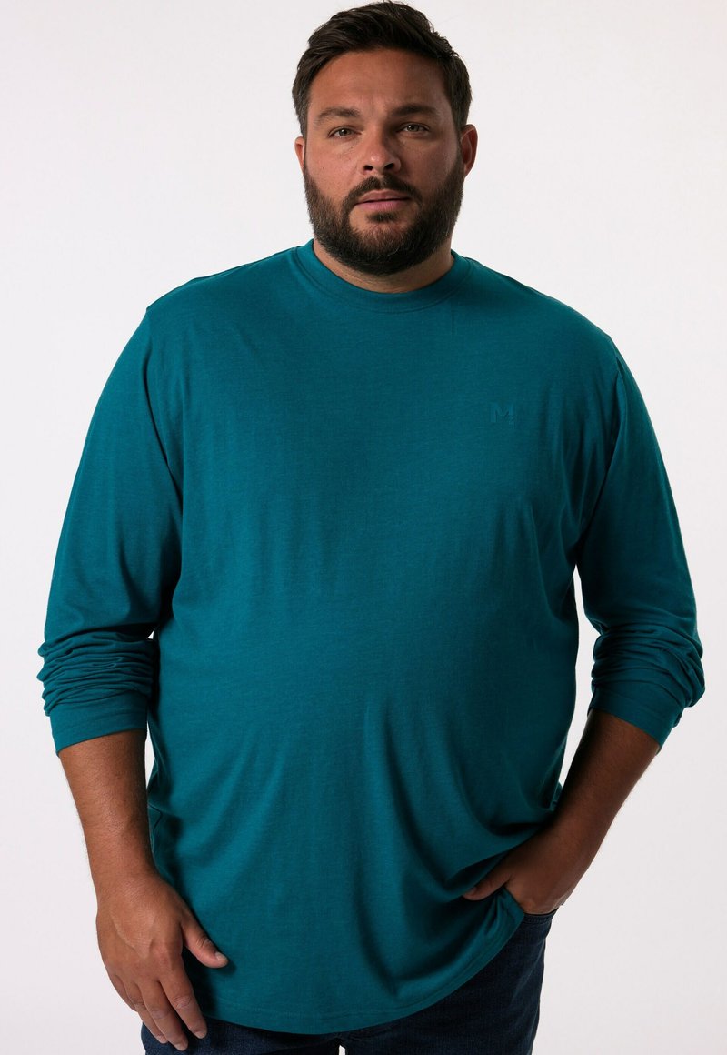 T-shirt à manches longues turquoise en tissu doux ; il présente un col rond, une coupe classique et un logo subtil sur la poitrine. Texture lisse.