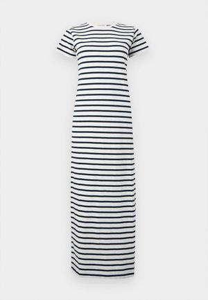Woman wearing a white and navy striped short-sleeve maxi dress, holding a black handbag, and wearing black open-toe heeled sandals.