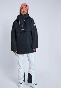 Svart vattentålig jacka med en framficka, vita snöbyxor och en rosa mössa. Anmärkningsvärda logotyper på jackan och byxorna.