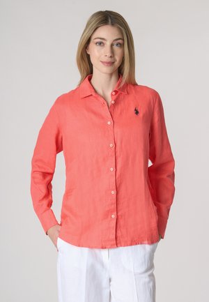 Camicia di lino corallo con maniche lunghe, chiusura a bottoni frontale e un piccolo logo blu navy sul petto. Tessuto morbido, design casual, orlo dritto.