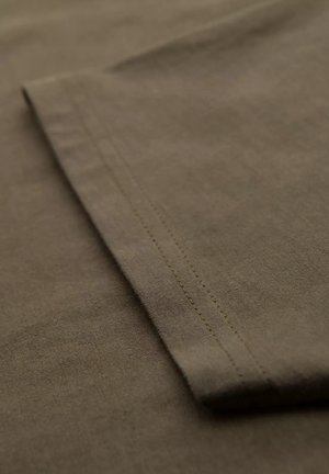 Olivengrønt bomuldsstof med en glat tekstur og en foldet kant. Synlig stitching langs sømmen tilføjer detalje.