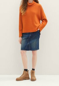 Oranžový žebrovaný rolák, džínová tužková sukně s šikmými švy, hnědé šněrovací kotníkové boty, nošené s černými ponožkami po kotníky.