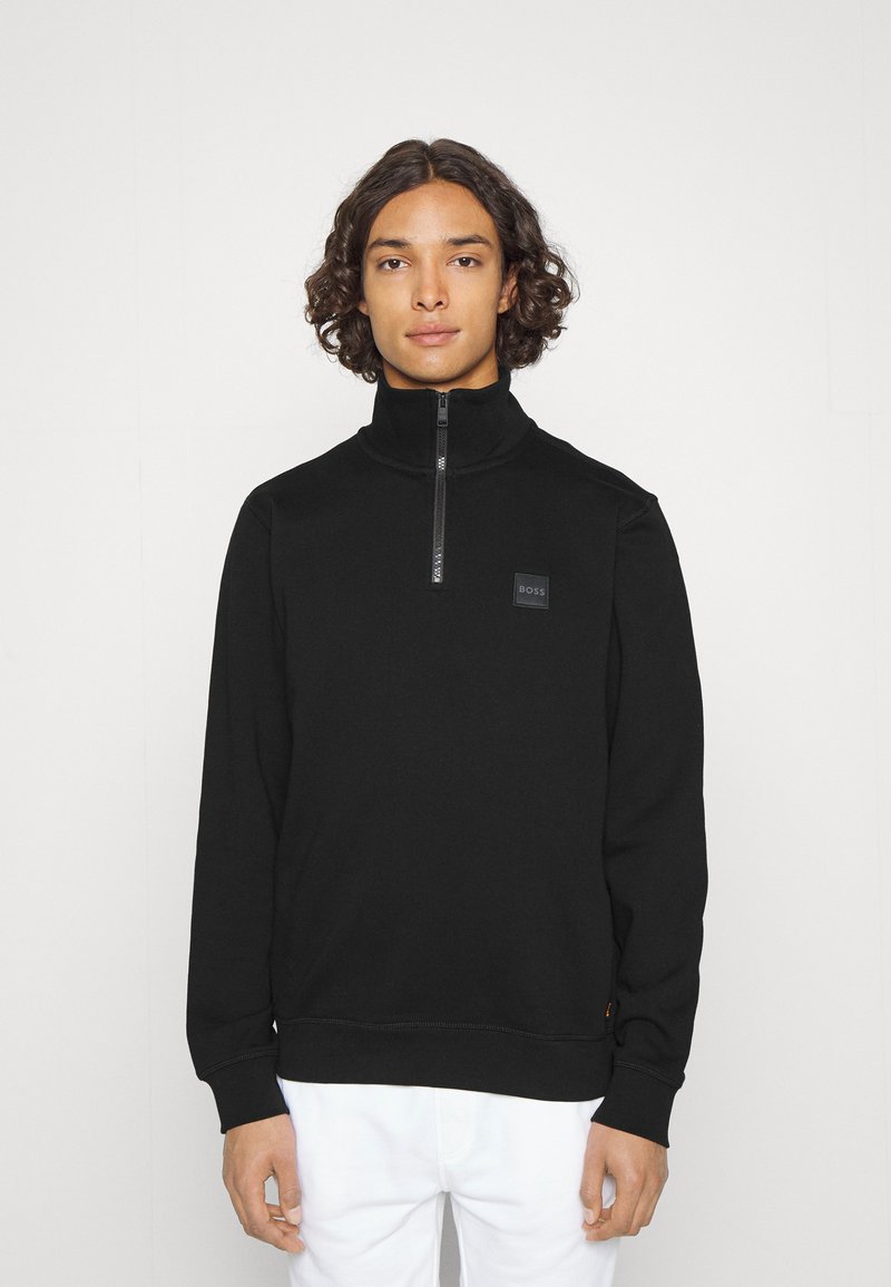 Zwarte ziphoodie met hoge kraag, textuurstof en een klein logopatch op de borst. Voorzien van ribgebreide manchetten en zoom.