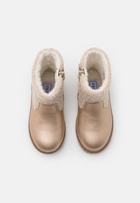 Botine din bronz cu un finisaj metalic neted și un guler din blană artificială texturată, având un fermoar lateral pentru a fi ușor de purtat.