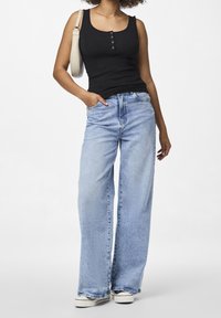 Svart ribbad tanktop med knapplayouter; ljusblå vida jeans med en blekt finish; vita sneakers; liten krämfärgad axelväska.