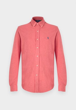 Hosszú ujjú, gombos ing korall színben, puha anyagból készült. Klasszikus gallérral és egy kis kék logóval rendelkezik a mellkason.