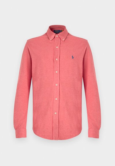 Ilga rankovė, mygtukais užsegama marškiniai koralinės spalvos, pagaminti iš minkštos medžiagos. Yra klasikinis apykaklė ir mažas mėlynas logotipas ant krūtinės.