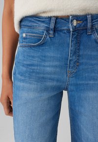 Jeans in denim azzurro chiaro con vita alta, caratterizzati da uno stile tradizionale a cinque tasche, leggera scoloritura e cuciture a contrasto.