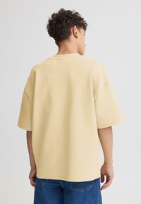 T-shirt en coton beige surdimensionné avec un col rond, des épaules tombantes et des manches courtes. Texture lisse, détails de couture minimalistes.