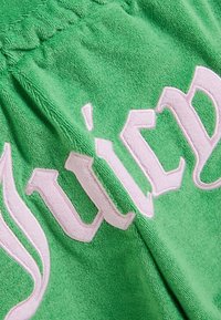 Πράσινο ύφασμα από πετσέτα με μεγάλα, ανοιχτό ροζ κεντημένα γράμματα που διαγράφονται κυρτά στην επιφάνεια.