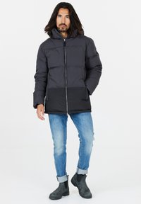 Svart puffjacka med dragkedja och huva, med en kontrasterande svart nederdel, i kombination med ljusblå jeans och svarta kängor.