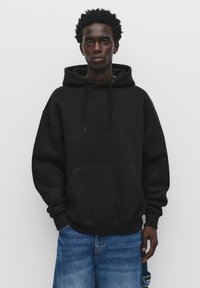 Black hoodie with drawstrings and a front pocket, relaxed fit, made of soft material, paired with light blue baggy jeans.