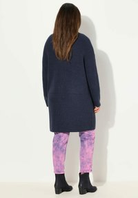 Marinblå stickad cardigan med sidofickor, bärs över rosa batikbyxor och svarta ankelstövlar, med en avslappnad passform och ribbad textur.