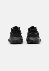 Black athletic shoes with a textured upper, rounded heel, and a rubber sole. Features pull tabs and contrasting stitching accents.