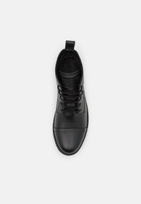 Black leather sneaker with textured upper, laces, and a pull tab. Sleek design features a rounded toe and minimalistic accents.