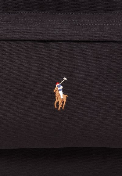 Logotipo bordado de un jugador de polo con pantalones blancos y camisa azul, montando un caballo marrón y sosteniendo un mallete levantado sobre una tela negra.