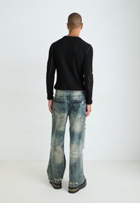 Abgetragenes schwarzes geripptes Langarmoberteil mit Muster auf den Ärmeln, kombiniert mit lockeren,Destroyed Jeans in hellblau im Schlagstil und schwarzen Plateaustiefeln.
