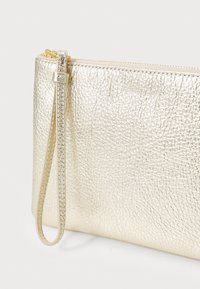 Pochette de soirée en métal doré, avec une surface texturée, une fermeture éclair et une bandoulière amovible. Forme rectangulaire compacte.