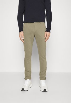 Chinos w jasnym beżowym bawełnianym materiale o slim fit. Zrolowane mankiety i kieszenie boczne. Połączone z białymi trampkami i granatowym swetrem z okrągłym dekoltem.