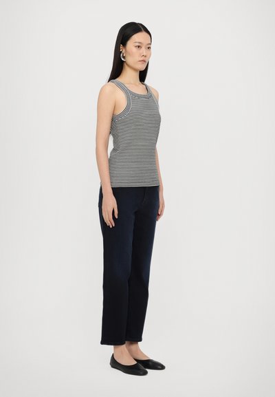 Stripet, ærmeløs tanktop i sort og hvid, parret med mørk denim straight-leg jeans og sorte flade sko. Simpel, tætsiddende design.