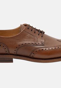 Chaussure en cuir brun à lacets avec une finition texturée, des perforations décoratives et un talon en bois empilé. Design classique de type "wingtip".