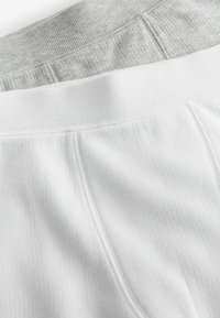 Witte en grijze katoenen onderbroeken met ribbelige elastische taillebanden, een gladde textuur en een gelaagd ontwerp dat beide kleuren toont.