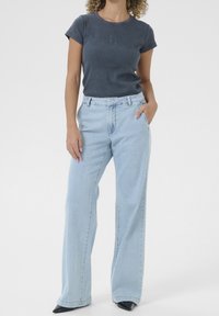 Vaaleansiniset leveät farkut, jotka on yhdistetty tummanharmaaseen istuvaan t-paitaan, jossa on hienovarainen kohokuvioitu logo, sileä rakenne ja rento istuvuus.