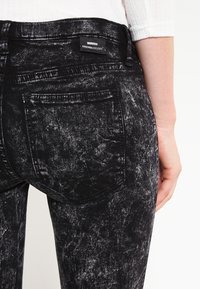Černé džínové kalhoty s texturovaným, opotřebovaným vzhledem. Mají dvě zadní kapsy, značkovou cedulku a střih na míru.