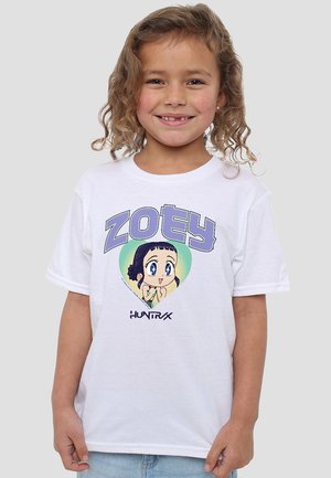 Lächelndes Kind mit lockigem Haar, das ein weißes T-Shirt trägt, auf dem ein Cartoon-Charakter in einem grünen Herzen zu sehen ist, mit dem Wort "ZOEY" darüber.